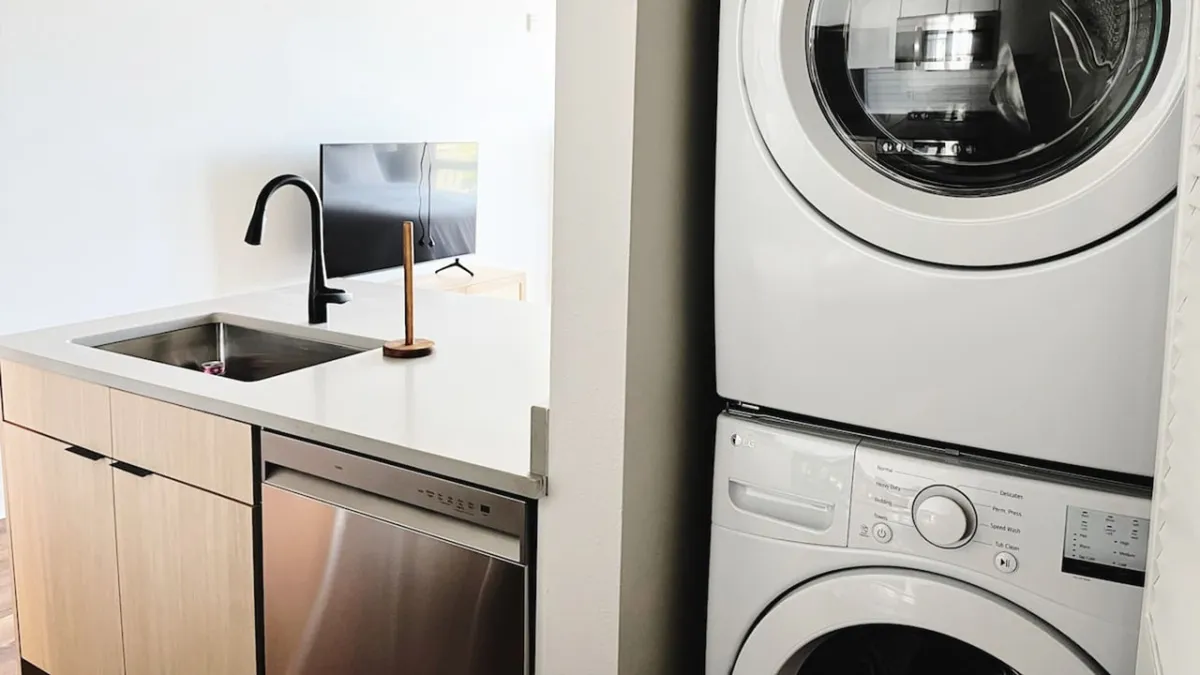 This image features a contemporary interior with a visible sink and washer/dryer unit, situated near a smooth surface that could hint at a kitchen or utility area. The mood is efficient and practical, echoing the space's utility for multitasking during daily routines.