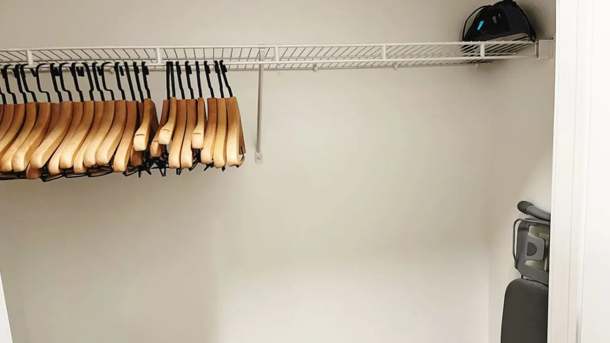 A functional, organized closet area featuring wooden hangers, a shelf, and additional storage items like a helmet and a vacuum cleaner. The space is practical yet accessible, emphasizing daily convenience for extended stays.